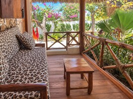 Terraza de madera con un sofá y una mesa, rodeada por barandilla de madera y abundante vegetación.