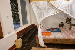 A room with a bed, a window, a wooden staircase, and a woven basket. - Salama & Mbuyuni Bungalows (Matemwe)