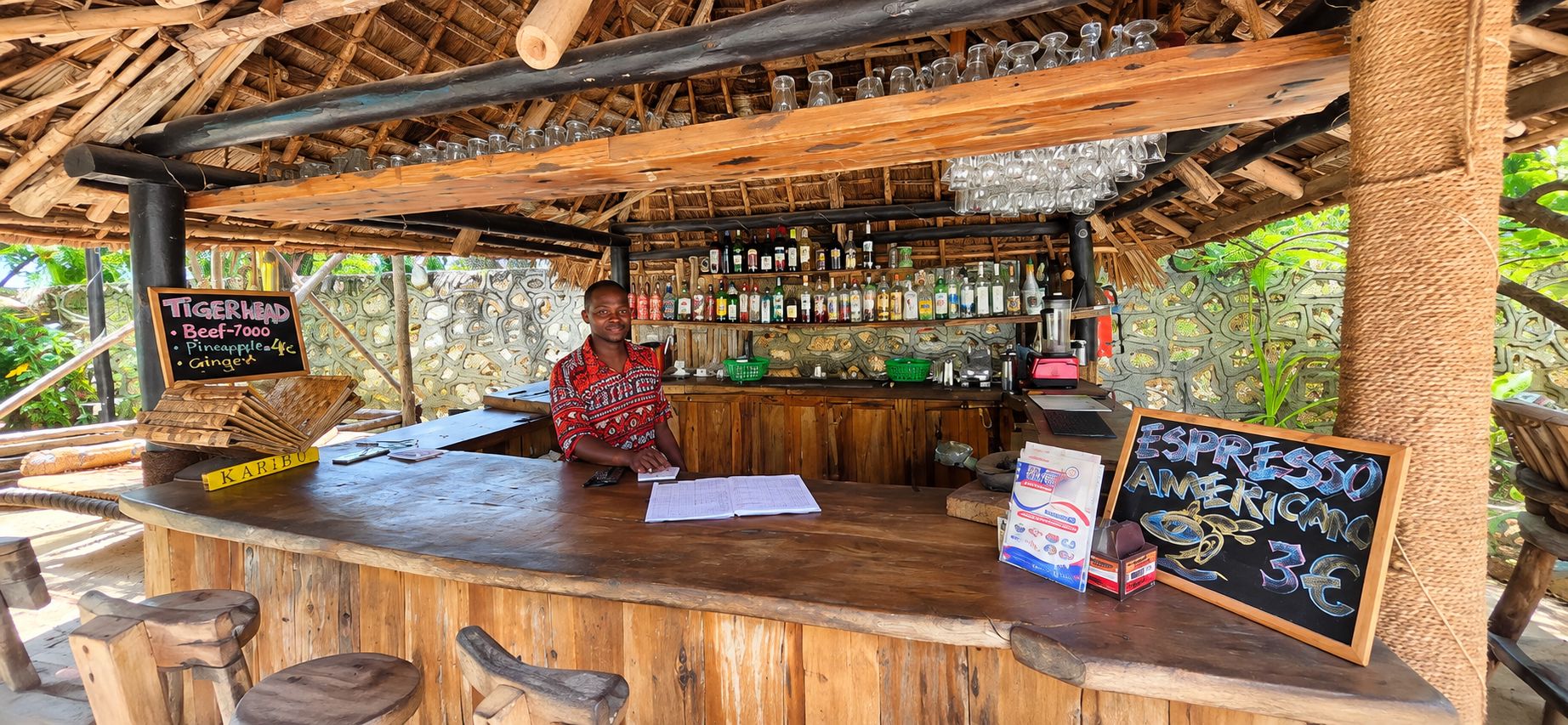 A rustic bar with wooden furniture and a thatched roof.