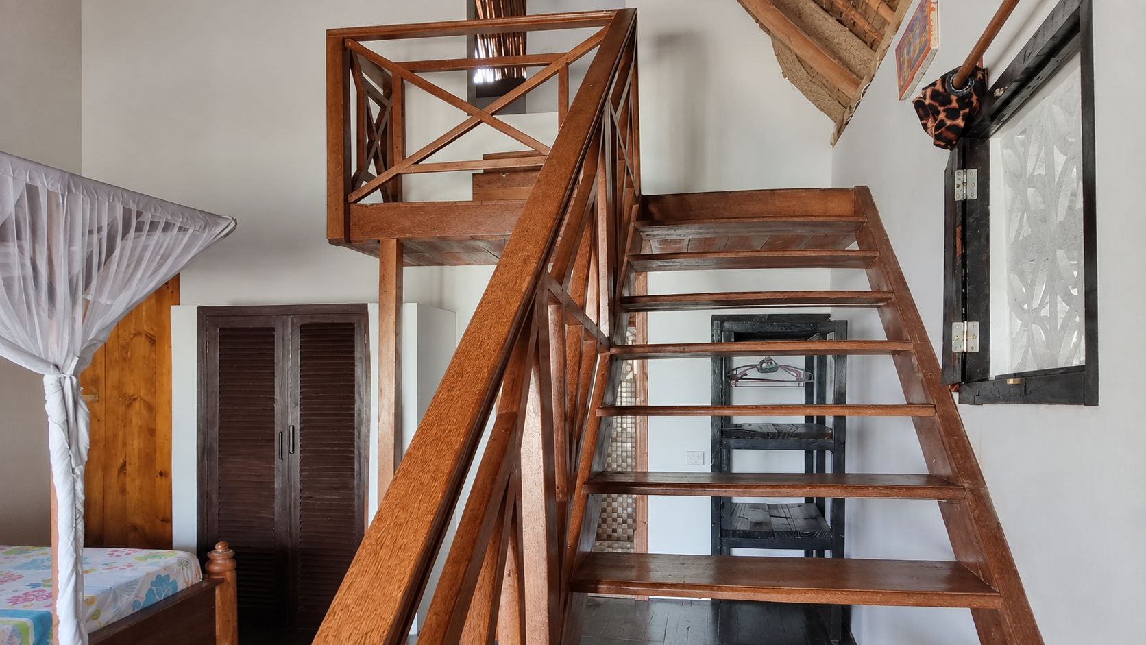A wooden staircase with a geometric design, a bed with a floral bedspread, and a wooden wardrobe.