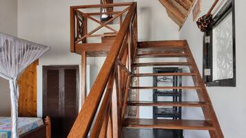 A wooden staircase with a geometric design, a bed with a floral bedspread, and a wooden wardrobe.
