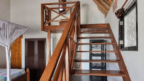 A wooden staircase with a geometric design, a bed with a floral bedspread, and a wooden wardrobe. - Salama & Mbuyuni Bungalows (Matemwe)