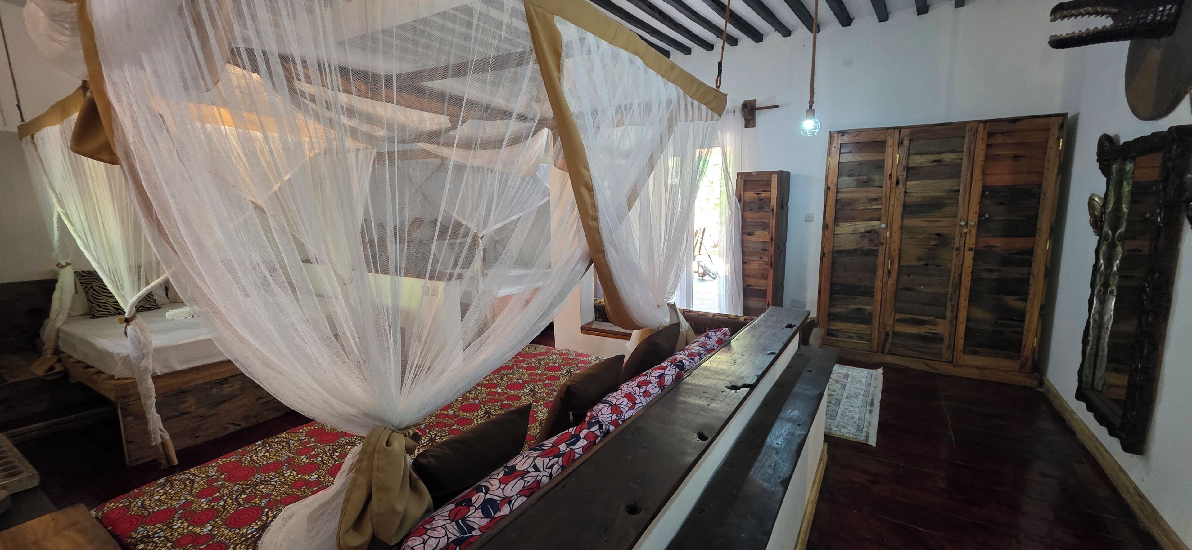Una habitación con una cama bajo un dosel, un banco de madera y una alfombra estampada.