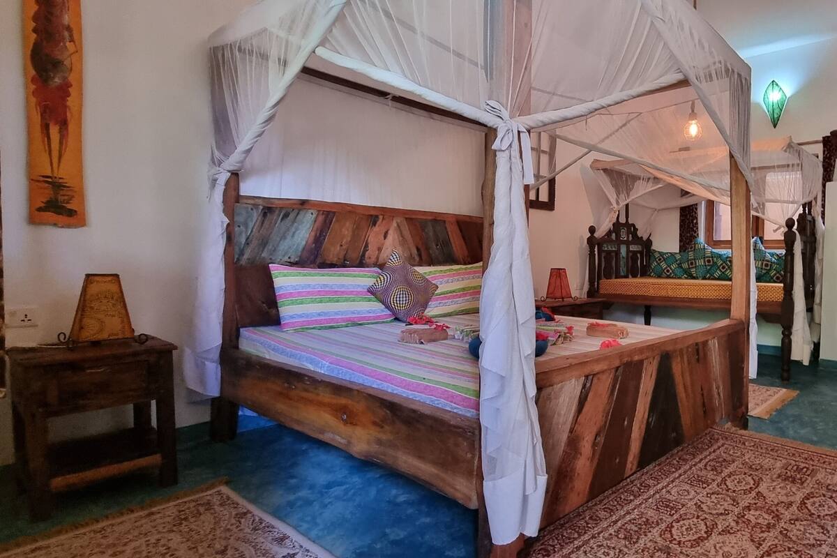 Una habitació amb un llit sota una bugada, una taula petita i una paret decorada amb obres d'art.