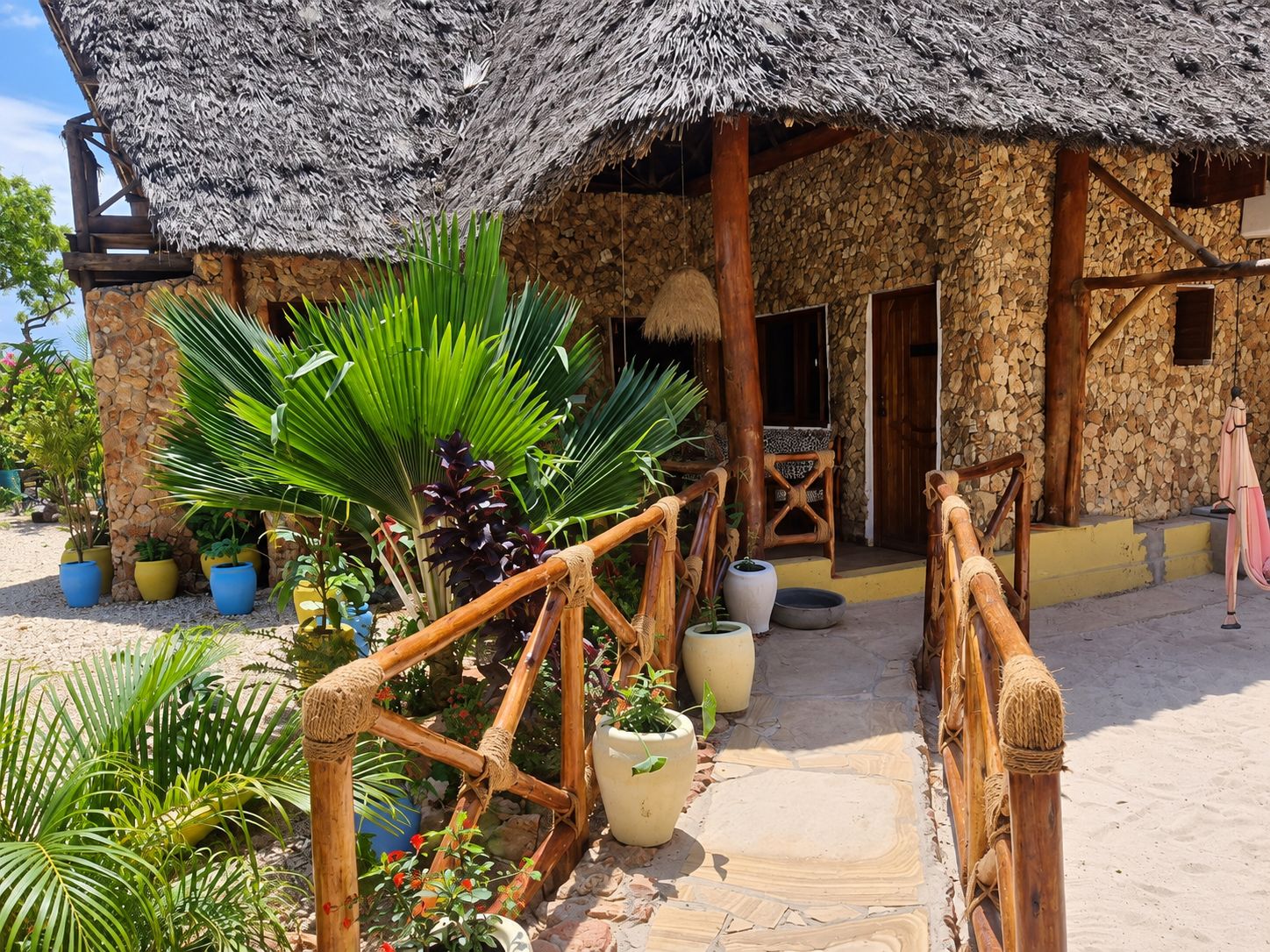 A rustic building with a thatched roof, surrounded by potted plants and a wooden fence.