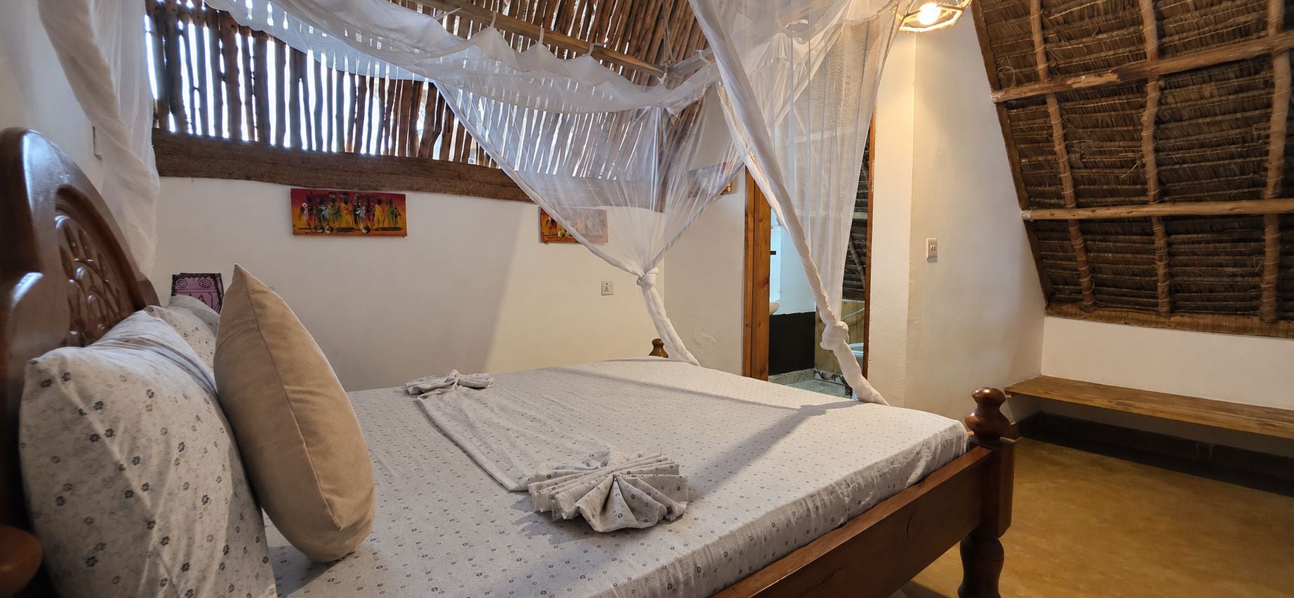 Una habitación con una cama, cabecero de madera, ventana con marco de madera y un cuadro colgado en la pared.