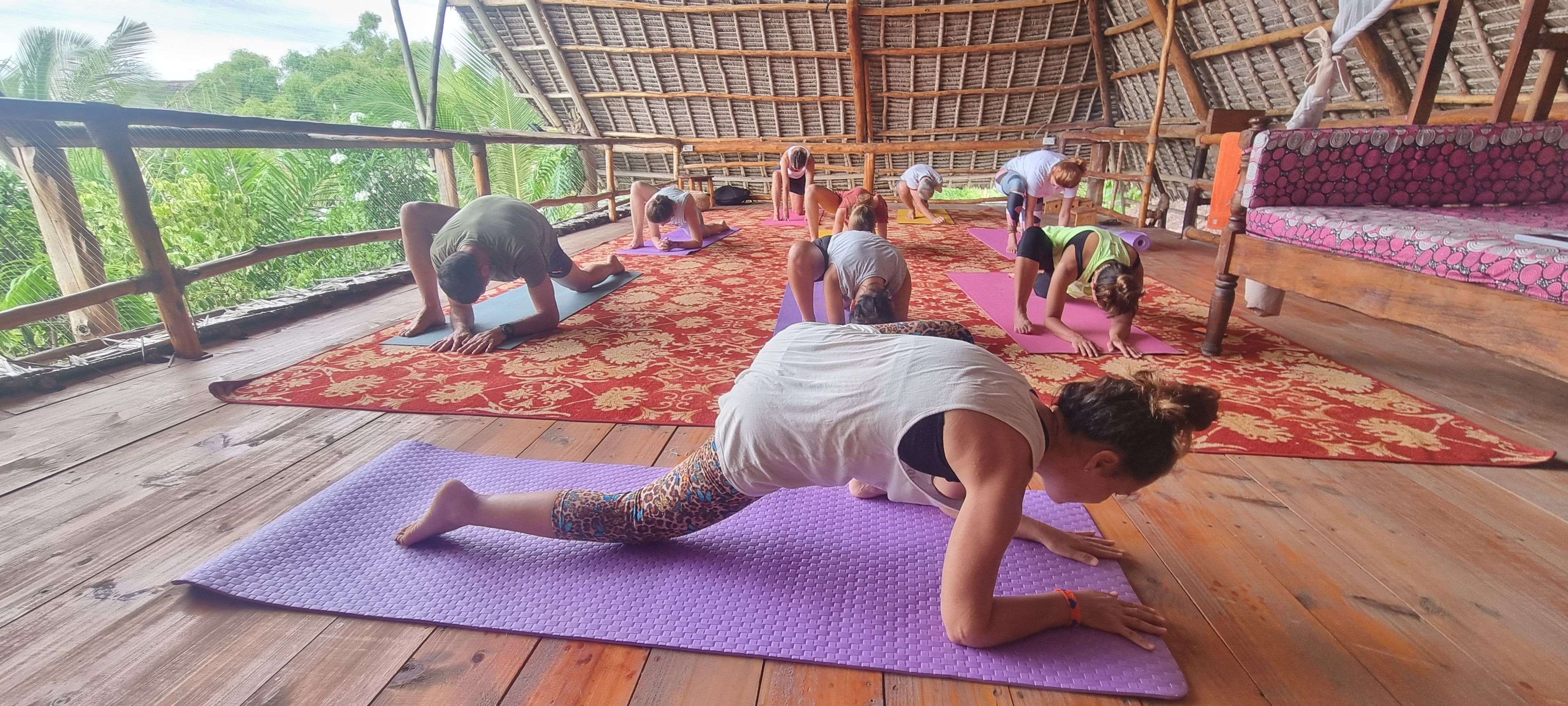 A group of people practicing yoga on mats in a wooden room with a thatched roof.