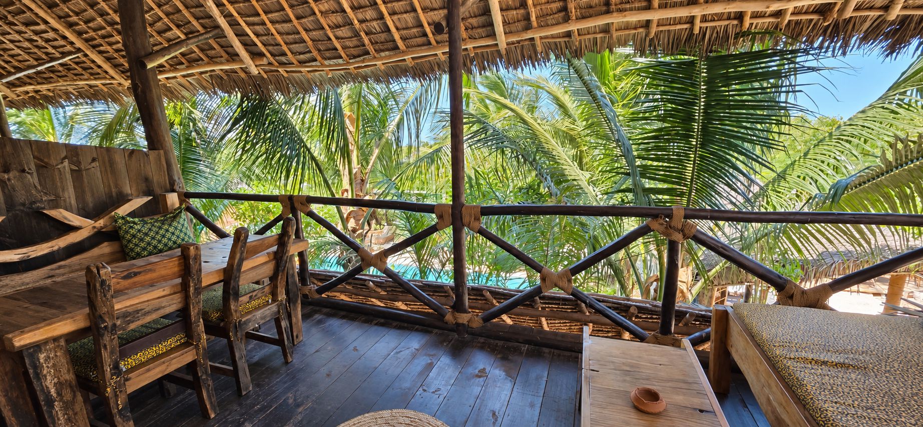 A wooden deck with a thatched roof, surrounded by palm trees.
