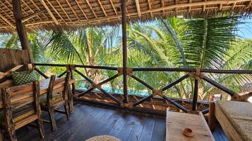 A wooden deck with a thatched roof, surrounded by palm trees.