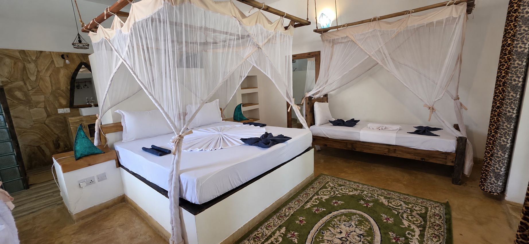 Ein Zimmer mit zwei Betten, jedes mit Baldachinvorhängen und Kissen. Auf dem Boden liegt ein grüner Teppich mit Muster.