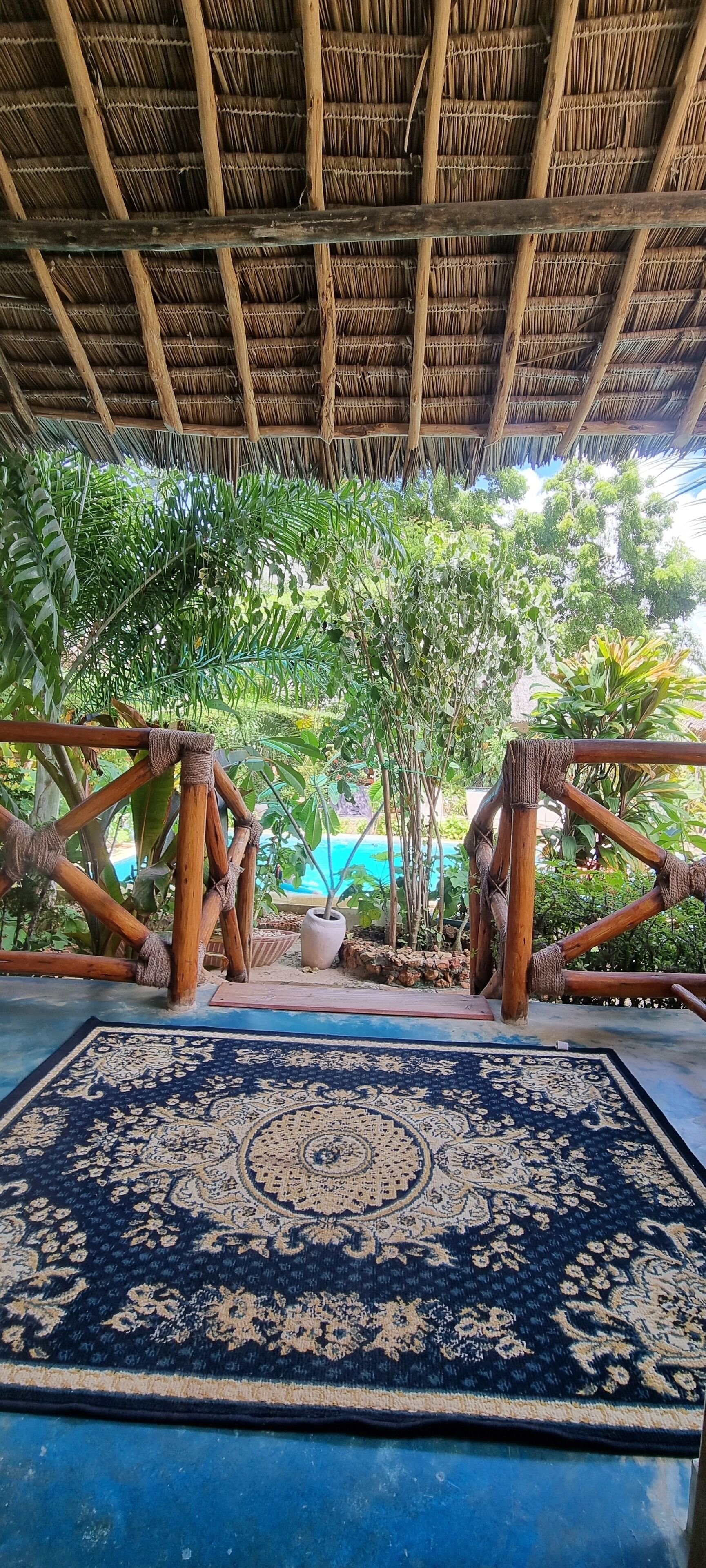Un espacio al aire libre cubierto con techo de paja, alfombra estampada y mobiliario de bambú.