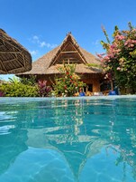 Una piscina cristalina con una construcción de techo de paja y exuberante vegetación tropical al fondo.