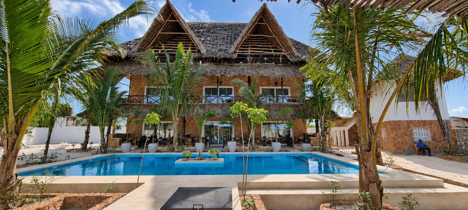 Ein Resort mit Pool, strohgedeckten Gebäuden und Palmen.