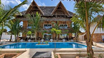 Ein Resort mit Pool, strohgedeckten Gebäuden und Palmen.