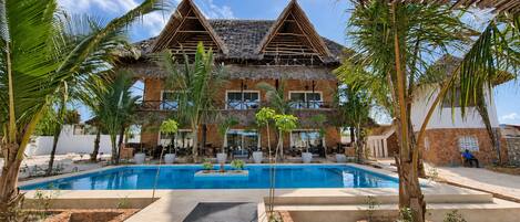 Un resort con piscina, edificios de techo de paja y palmeras.