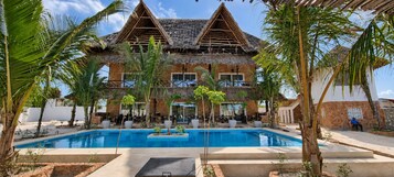 Un resort con piscina, edificios de techo de paja y palmeras.