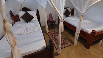 A room with two wooden beds, each with a canopy. There is a small table with a lamp between the beds.