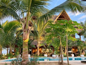 Een resort met een zwembad, palmbomen en een gebouw met rieten dak.