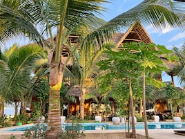 Un resort con piscina, palmeras y un edificio de techo de paja.