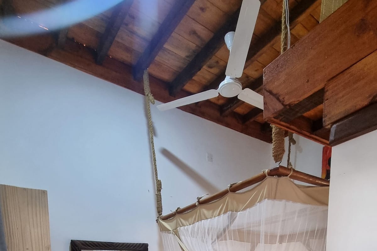 Habitació rústica amb terra de fusta, un llit amb mosquiter i una panxa de cavall de fusta, i un mirall a la paret.