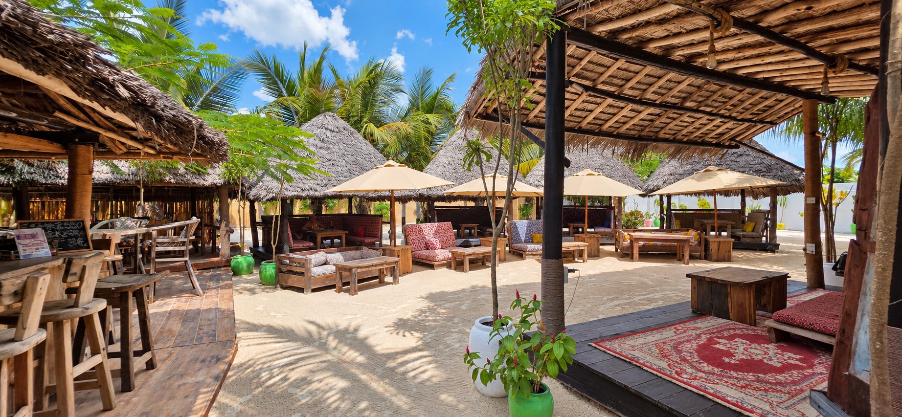 An outdoor seating area with thatched-roof structures, wooden furniture, and potted plants.