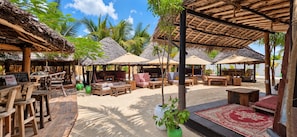 An outdoor seating area with thatched-roof structures, wooden furniture, and potted plants. - Salama & Mbuyuni Bungalows (Matemwe)