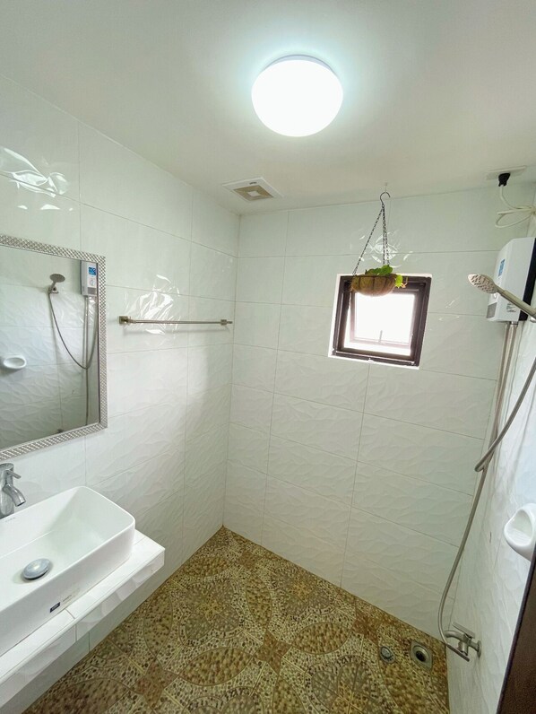Une salle de bain avec un lavabo blanc, un miroir, une douche et une petite fenêtre.