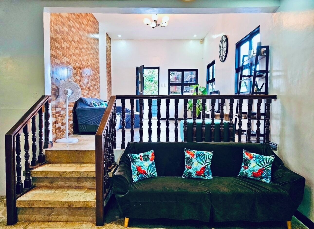 A staircase leading to a living area with a dark green sofa and colorful cushions, a wooden railing, and a view of the outside through open doors.