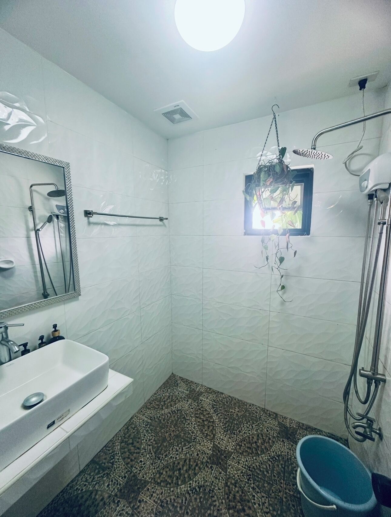 Un baño con lavamanos blanco, espejo, ducha y baldosas de suelo con diseño.