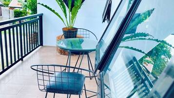 A balcony with a glass table and chairs, a potted plant, and a view of a building and trees.