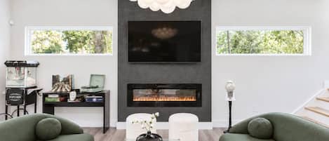 A modern living room with a flat-screen TV, fireplace, green sofas, and a chessboard.