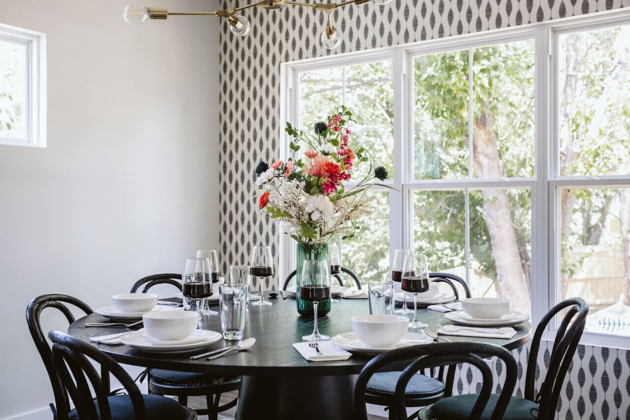 A dining table set for six with a vase of flowers in the center, surrounded by chairs.