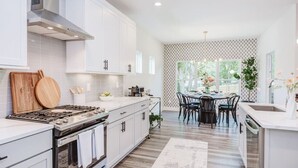 Una cocina moderna con armarios blancos, estufa a gas y un comedor con mesa y sillas.