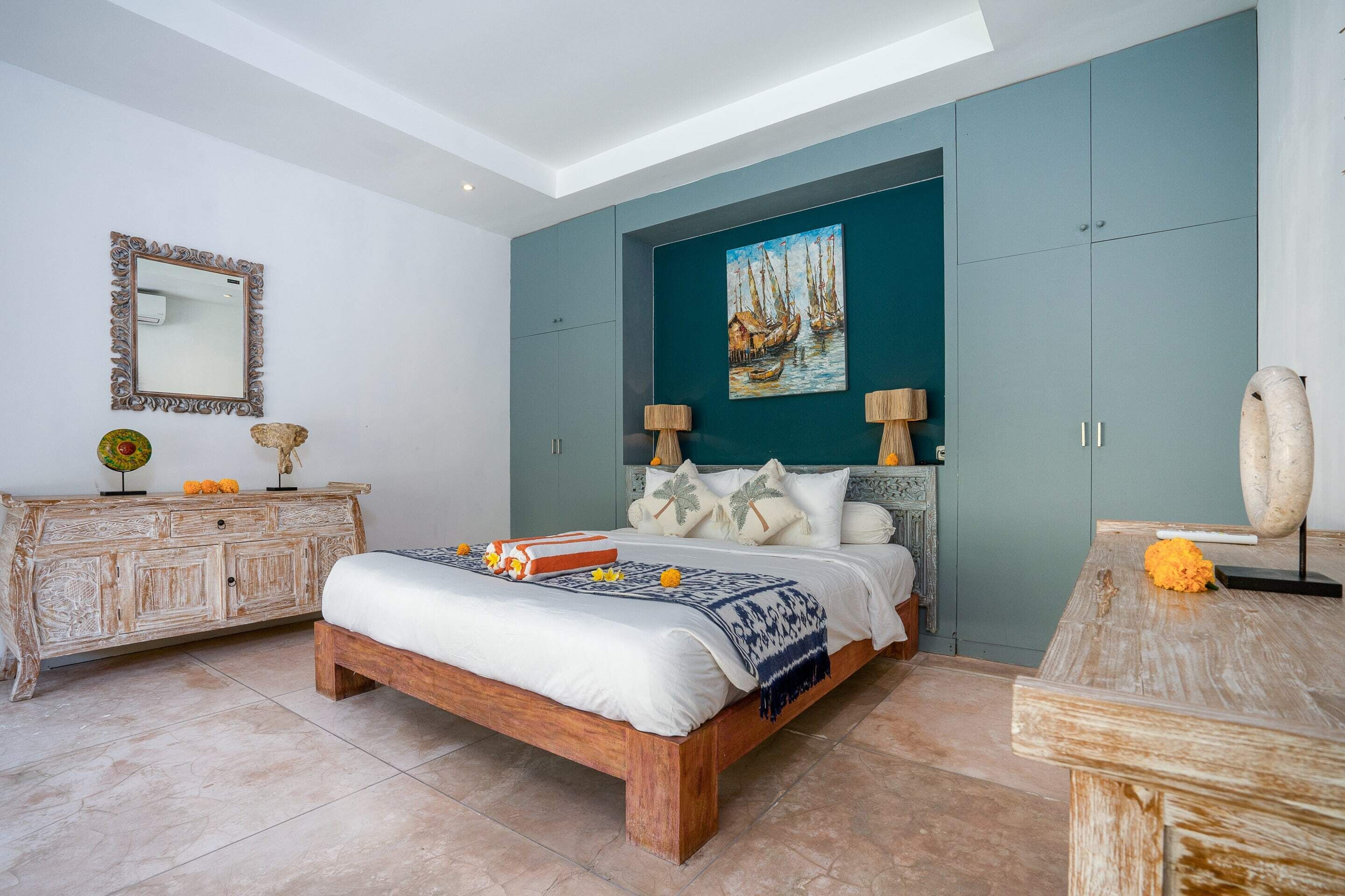 A bedroom with a wooden bed, a teal accent wall, and a painting of sailboats.