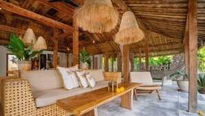 Un espacio al aire libre techado con mesa de madera, sofá de mimbre y sillas.