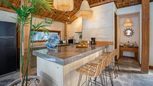 Una cocina con isla central, taburetes de bar, lámparas colgantes y una planta de bambú.