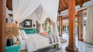 Un dormitorio amplio con cama con dosel, una mesita de noche azul turquesa y un gran ventanal con vistas a una zona de piscina.