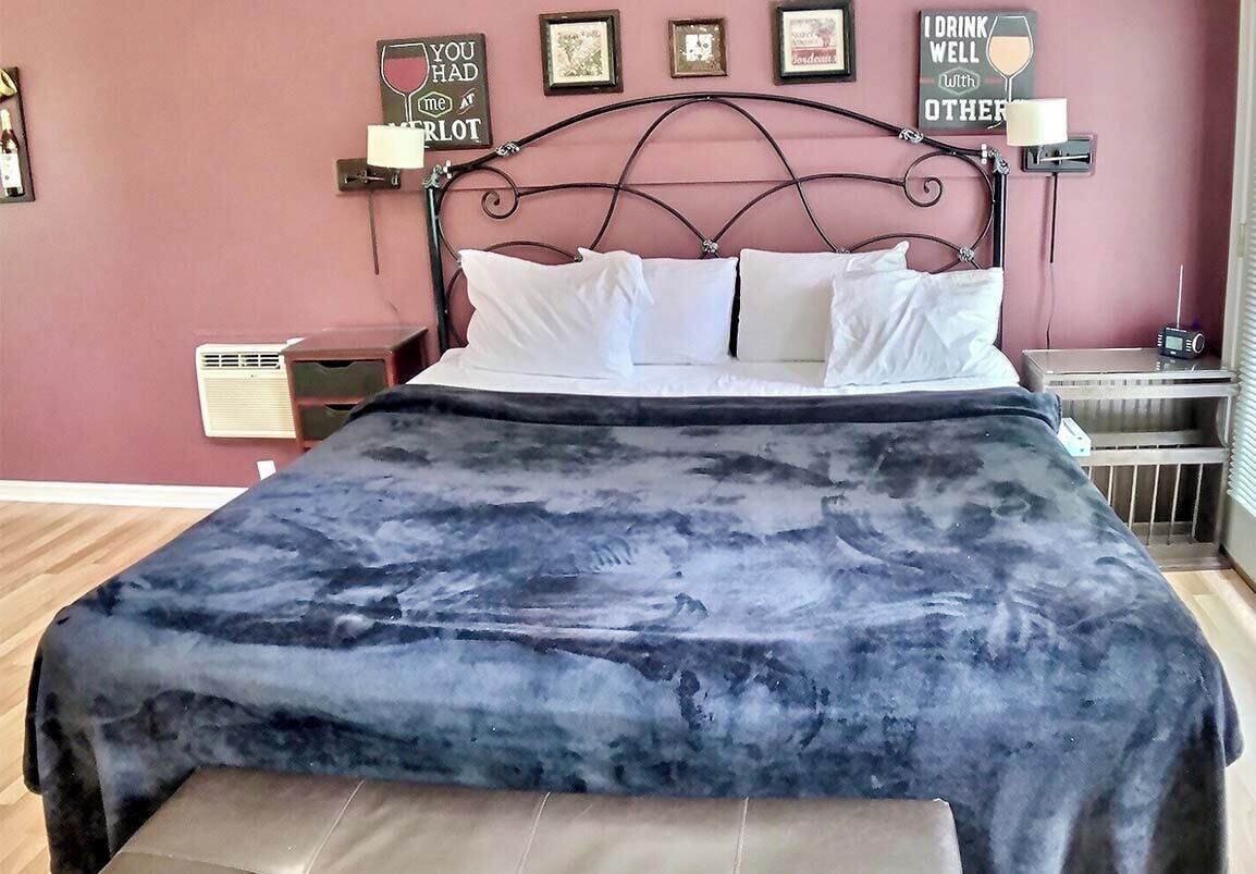 Un lit recouvert d’une couverture bleu foncé, avec une tête de lit en métal et des oreillers blancs. On peut voir des décorations murales et une petite table avec une lampe.
