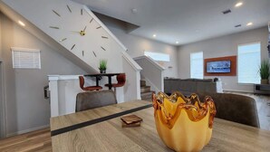 Un salon moderne avec un coin repas, comprenant un escalier, une horloge, un téléviseur et un vase décoratif.