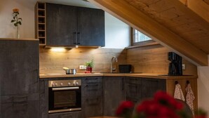 Una cucina moderna con mobili scuri, forno integrato e soffitto in legno.