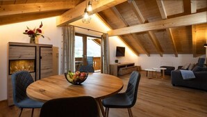 Un'accogliente sala da pranzo con pavimento in legno, un tavolo rotondo e sedie, una ciotola di frutta e vista all'esterno attraverso una grande finestra.