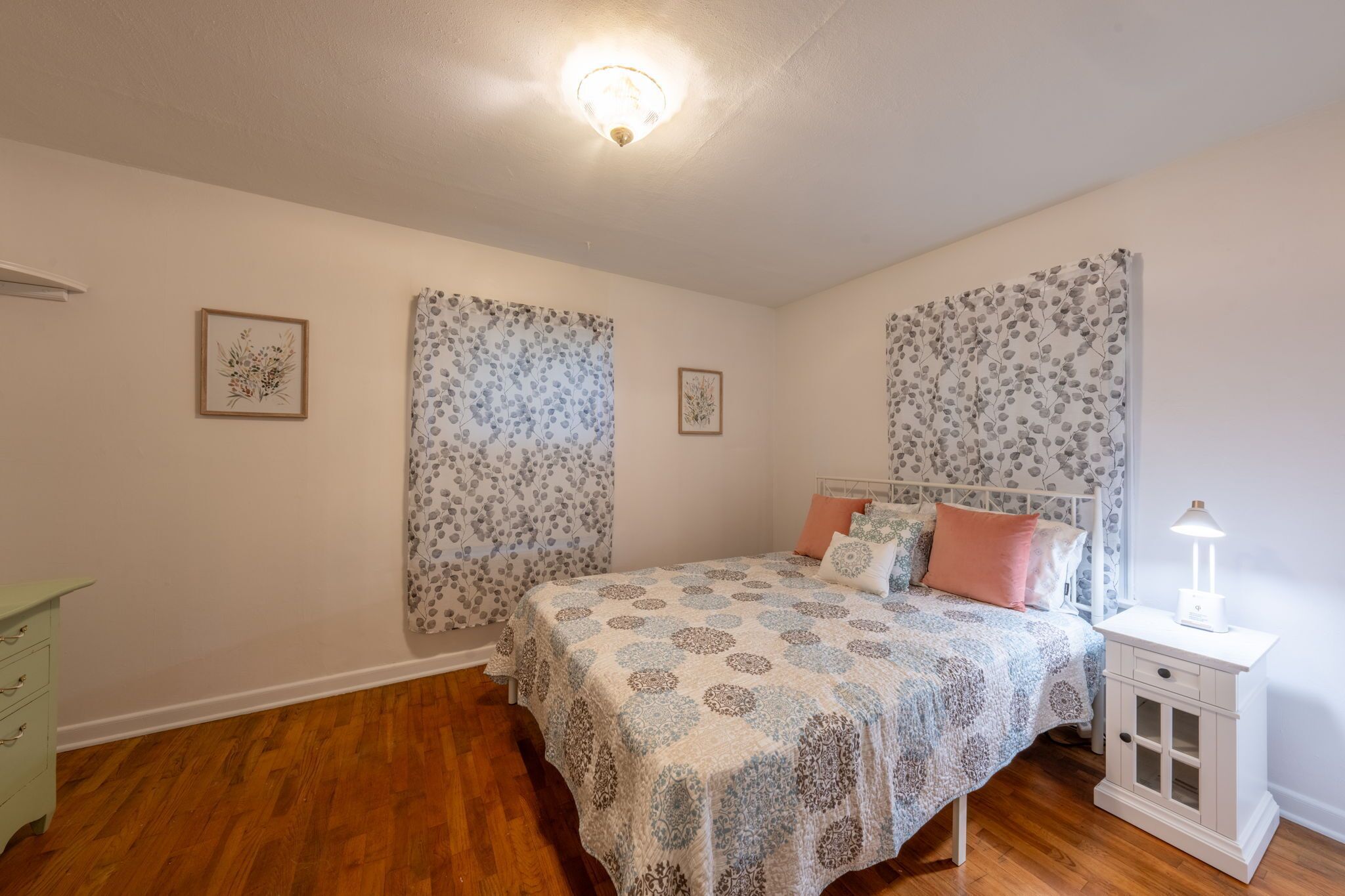 A bedroom with a bed, a nightstand, a dresser, and two framed pictures on the wall.