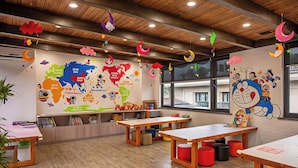 Ein Klassenzimmer mit einer Weltkarte, Lehrmaterialien und einer Zeichentrickfigur. Tische und Hocker sind für Sitzplätze angeordnet.