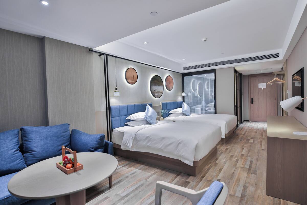 A modern hotel room with a large bed, a sofa, a small round table, and a desk.