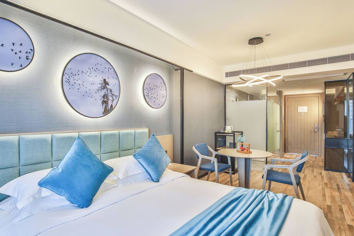A hotel room with a bed, two chairs, a small table, and a mirror.