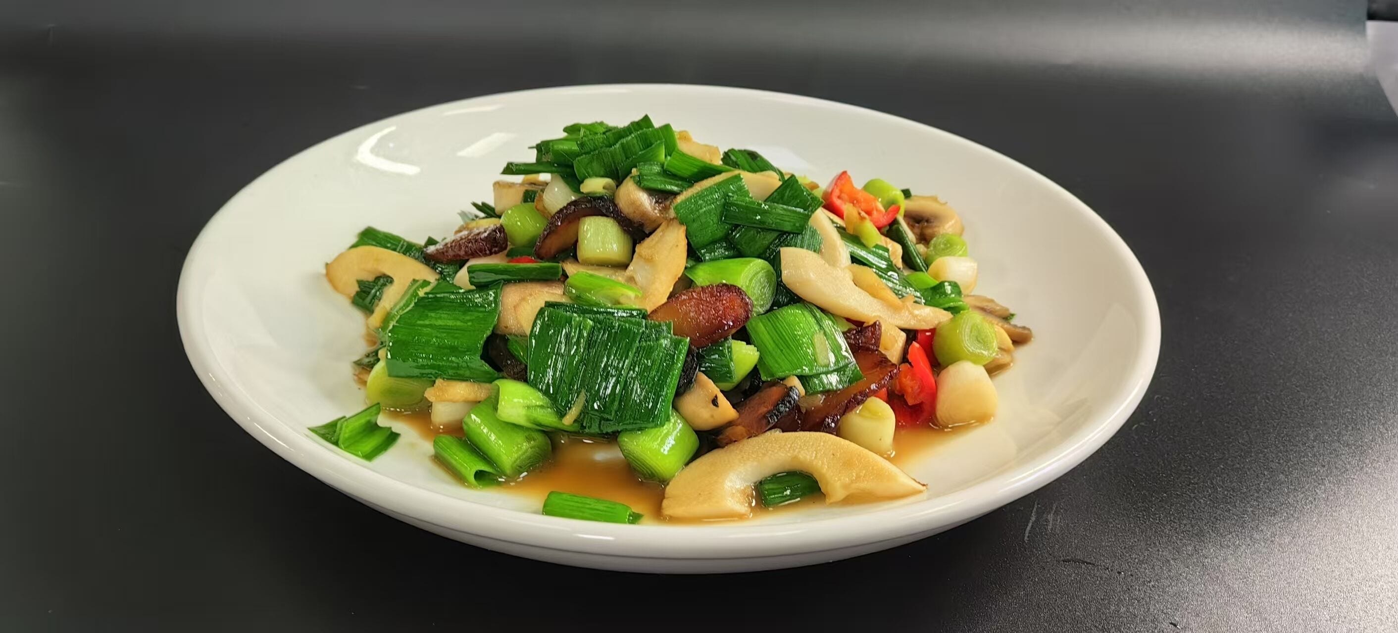 A white plate with a stir-fry dish containing vegetables and meat, served on a black table.