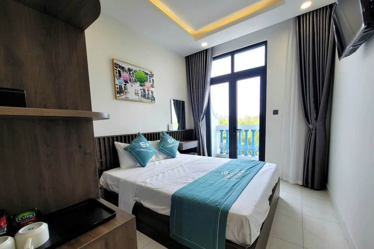 Une chambre d’hôtel avec un lit, une table de chevet sur laquelle se trouve un plateau avec divers objets, une fenêtre avec des rideaux et un balcon donnant sur une vue agréable.