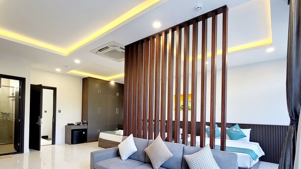 A modern hotel room with a grey sofa, a black coffee table, a wooden partition, and a bed with pillows. - E3 Homestay & Cafe Phu Quoc (Phu Quoc)