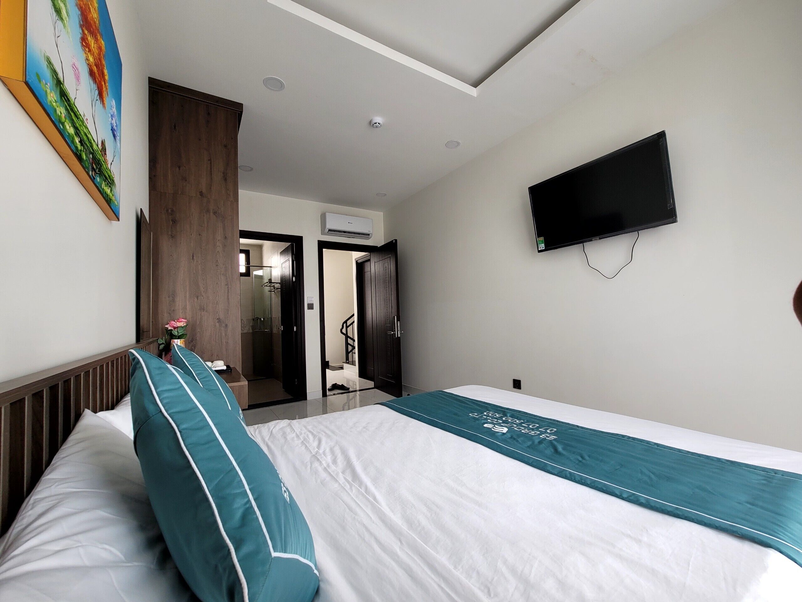 A hotel room with a bed, a TV mounted on the wall, and a shower area visible through an open door.