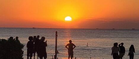 Atardecer sobre el océano, con siluetas de personas en una playa.